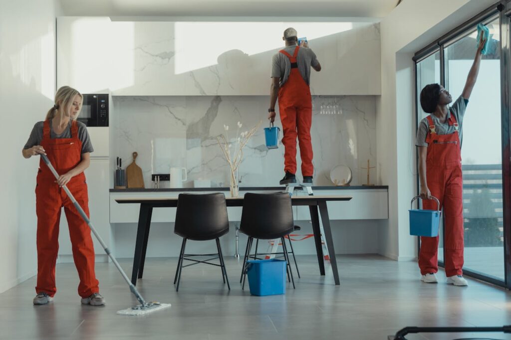 pexels-photo-6197108 Group of cleaners in red uniforms mopping and wiping glass in a modern dining room.